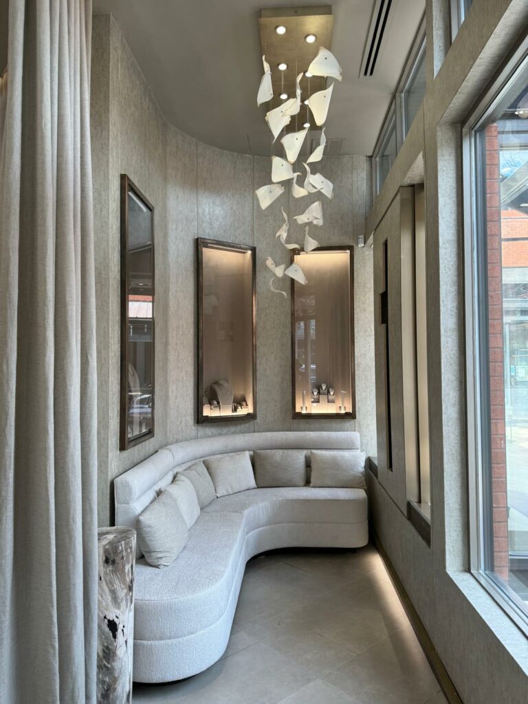 A modern seating area featuring a curved white sofa with cushions. The walls have light-colored decor and two framed mirrors. A pendant light made of white materials hangs from the ceiling, casting soft light into the space.